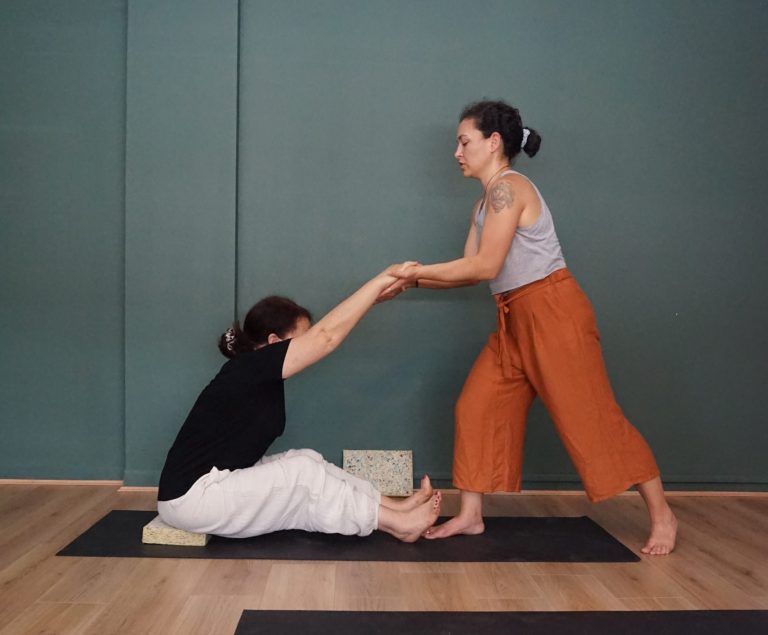 A Yoga beginners student practices a seated posture supported and assisted by a Yoga teacher